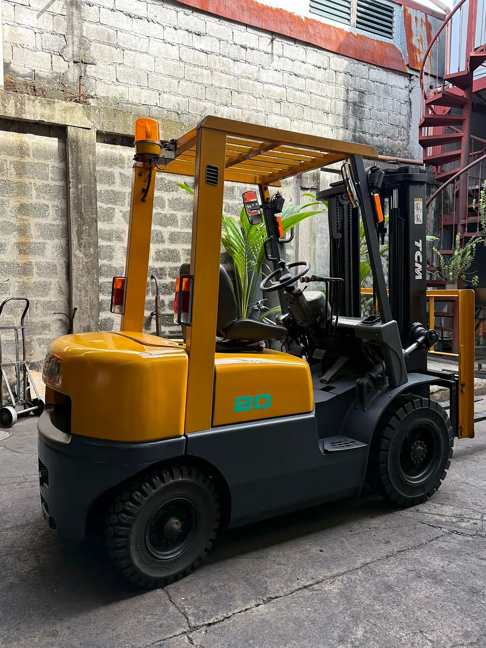 TCM 20 forklift with an amber beacon light, parked beside a block wall